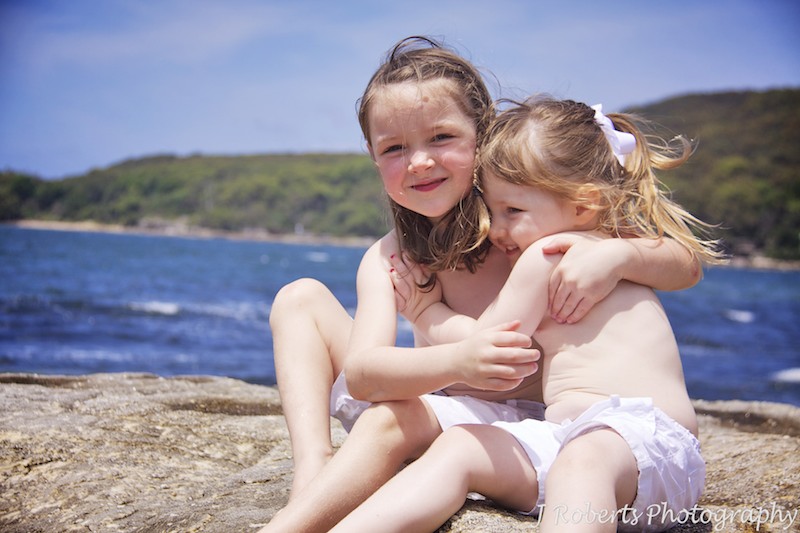 Sisters hugging on the rocks at the beach - family portrait photography sydney